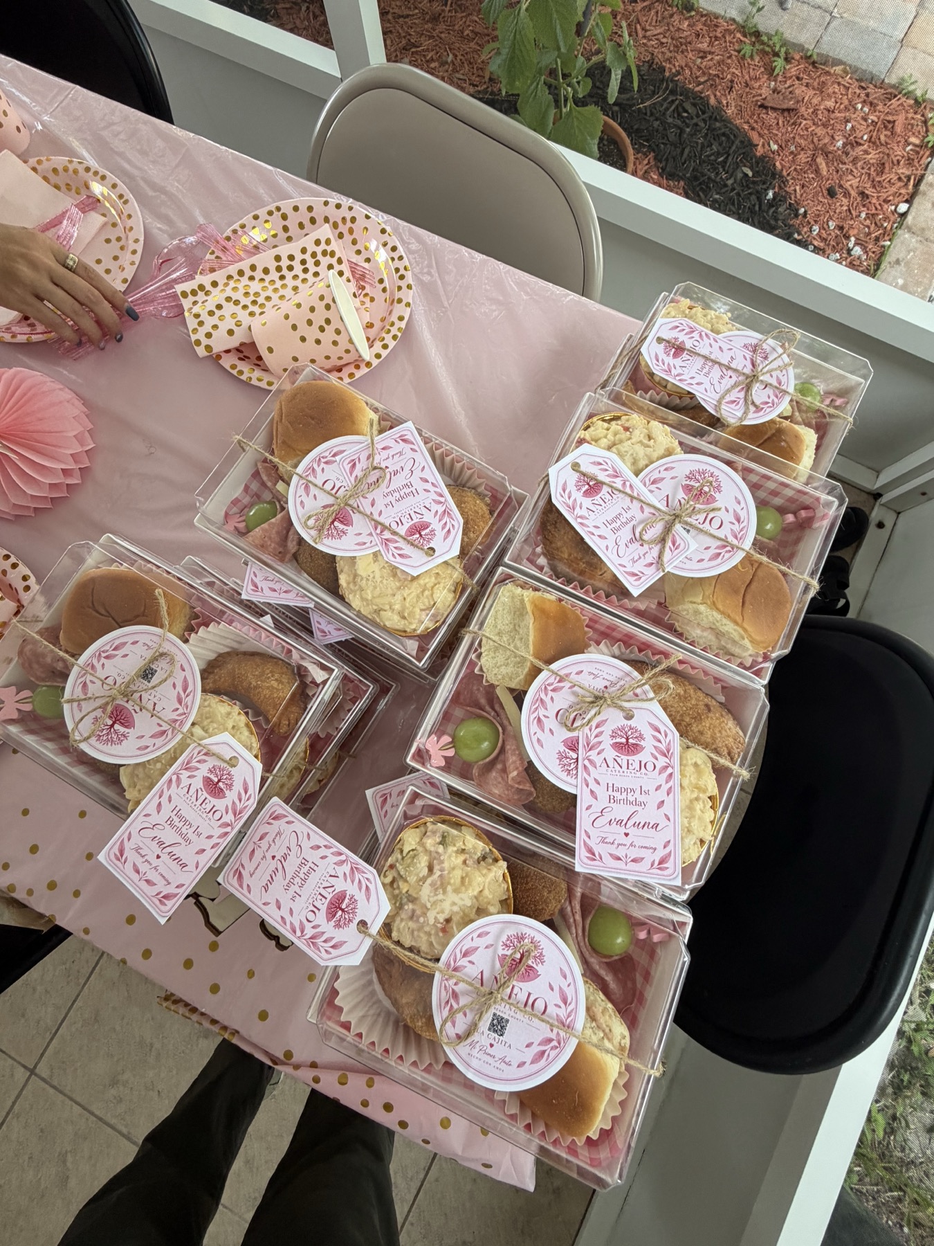 Multiple personalized pink first-birthday Cajitas arranged on the event table